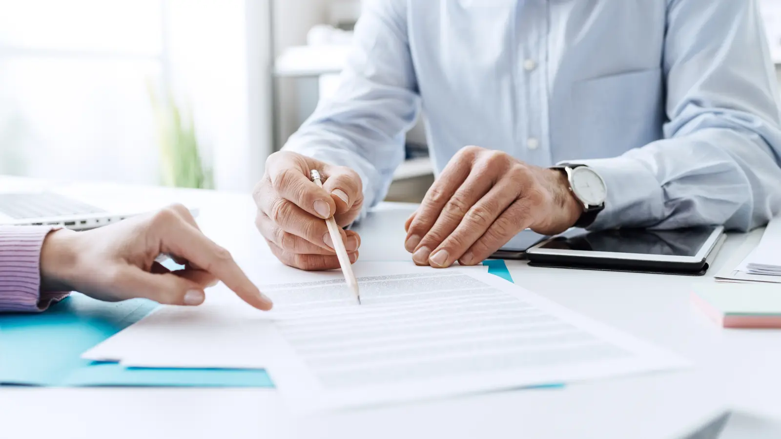 Un dirigeant d'entreprise et une courtière comparent deux contrats d'assurance posés sur une table de réunion.